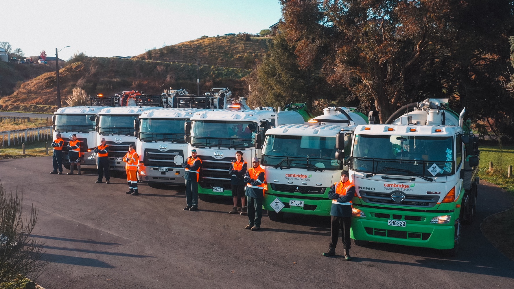 Two men, one wearing a hi-vis jacket with Waimea Group on the back, talking in front of an orange hydrovac being operated on a worksite.