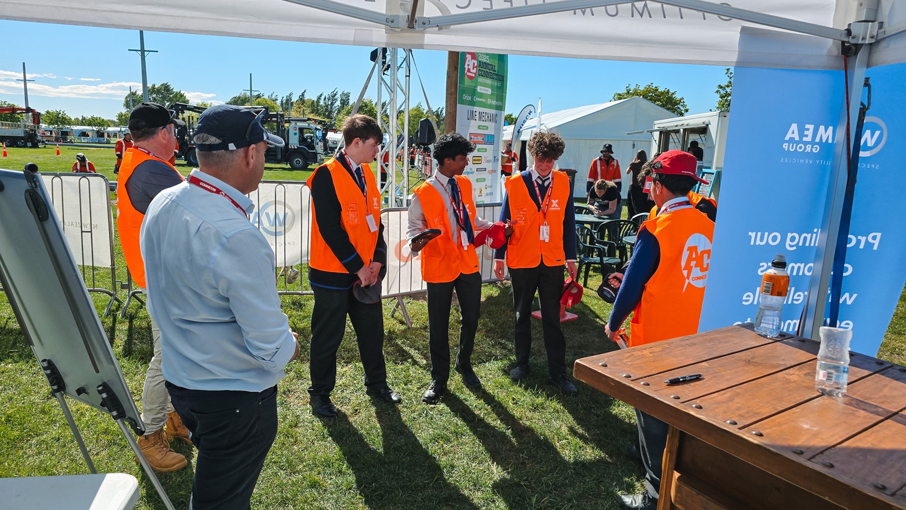 A showground viewed from up high, with lots of lines crane trucks set up with their crews demonstrating next to power poles, and stalls around the edge of the grounds, early in the morning.
