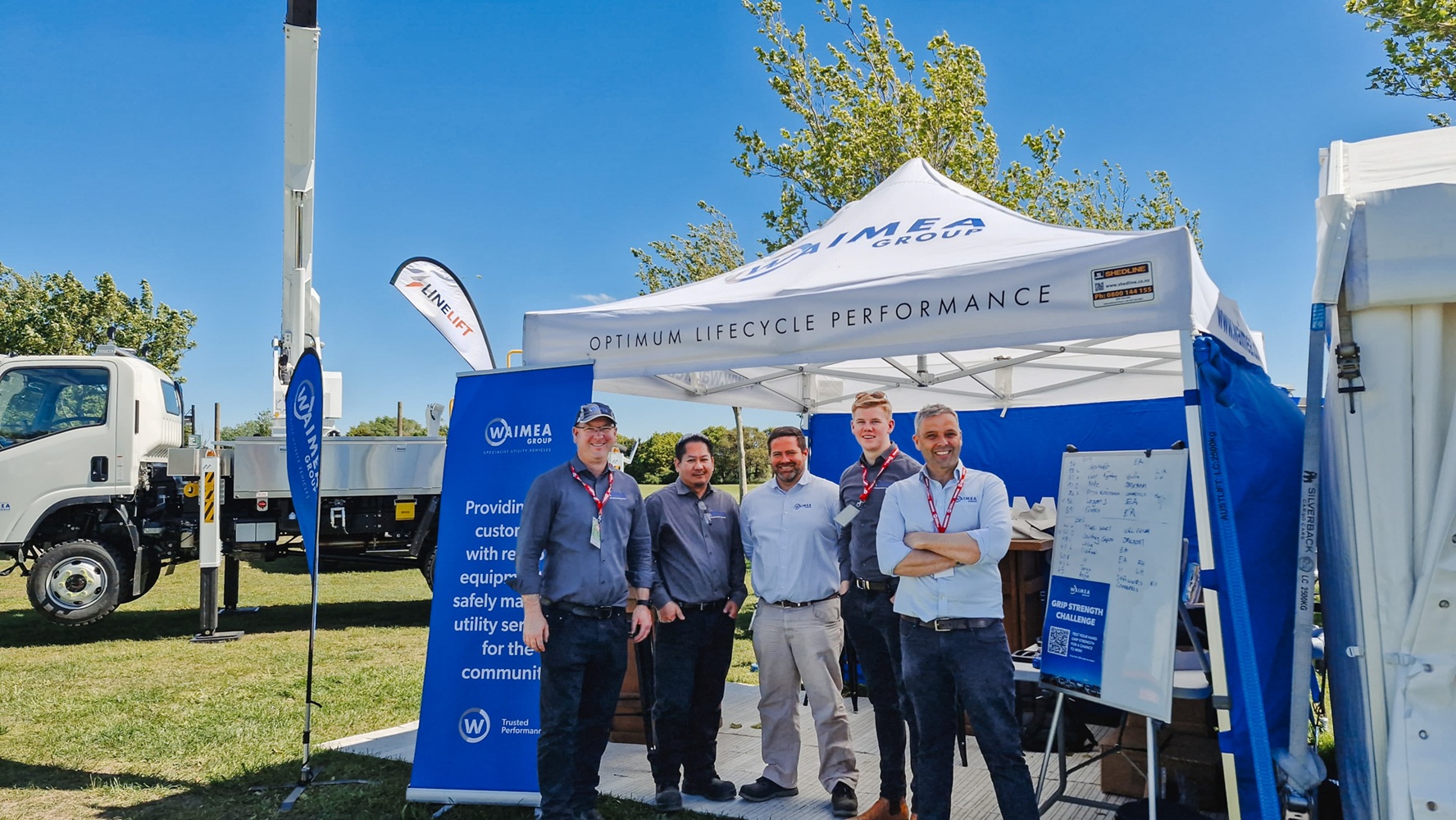 A showground viewed from up high, with lots of lines crane trucks set up with their crews demonstrating next to power poles, and stalls around the edge of the grounds, early in the morning.