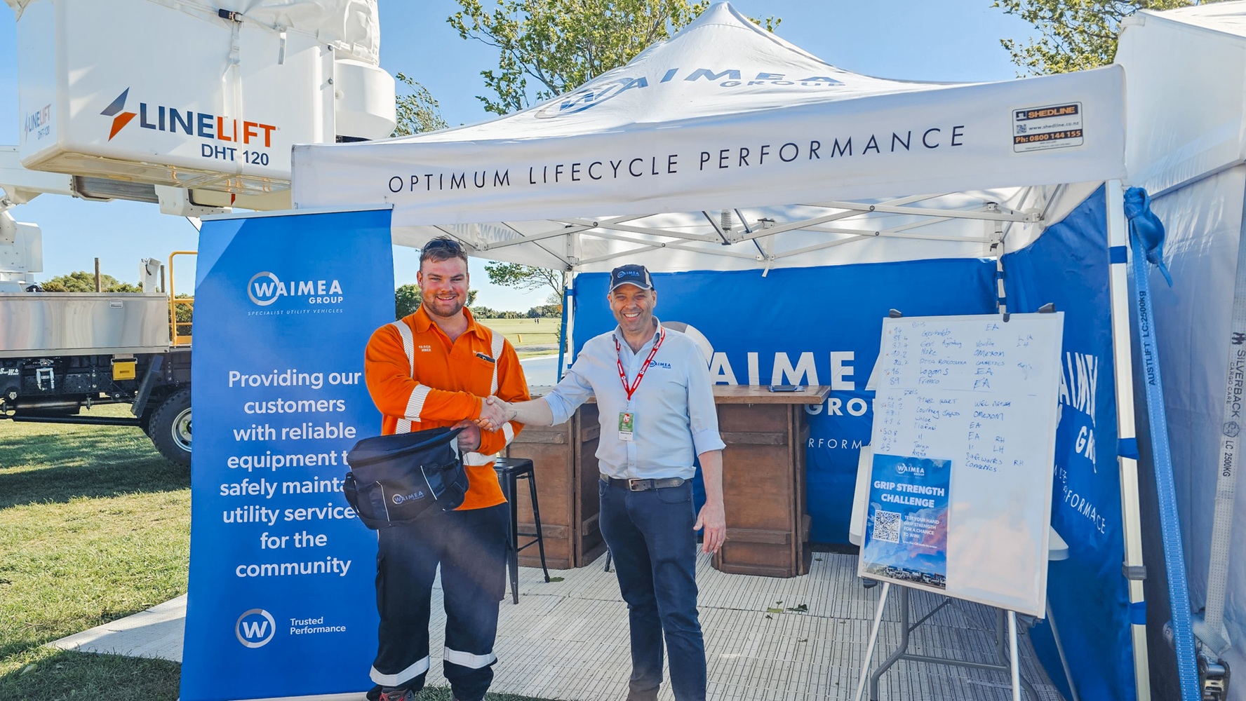 A showground viewed from up high, with lots of lines crane trucks set up with their crews demonstrating next to power poles, and stalls around the edge of the grounds, early in the morning.